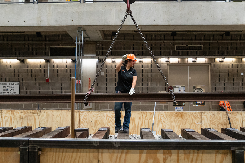 student guides a rail suspended by a crane over an indoor test track. 
