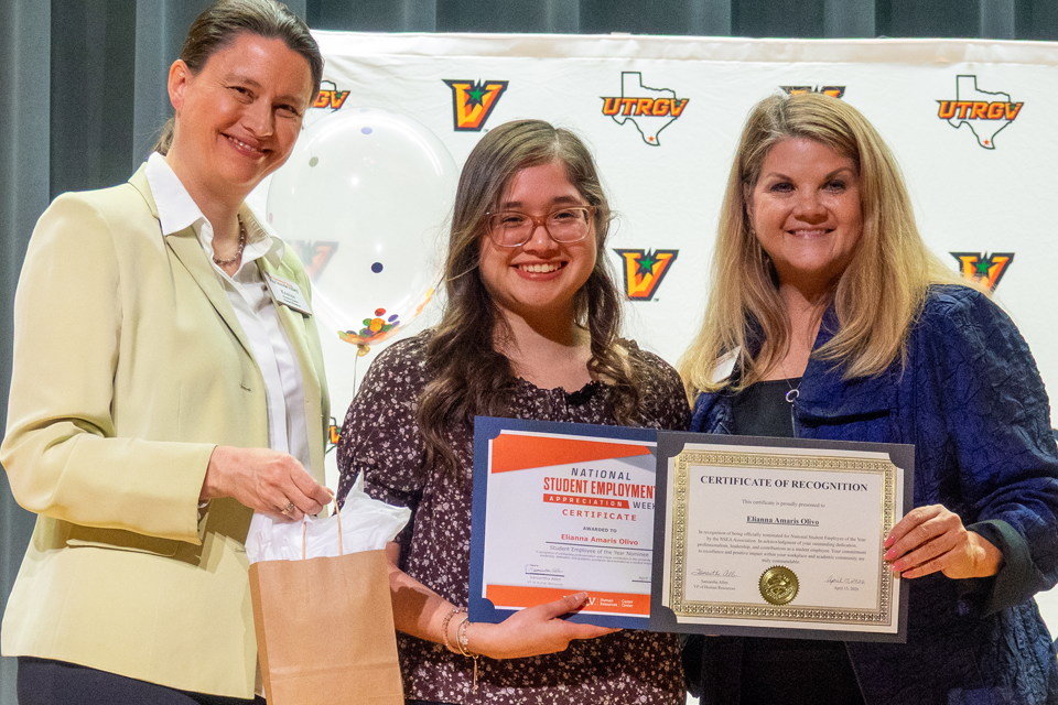 Three people standing on stage with one person holding an award