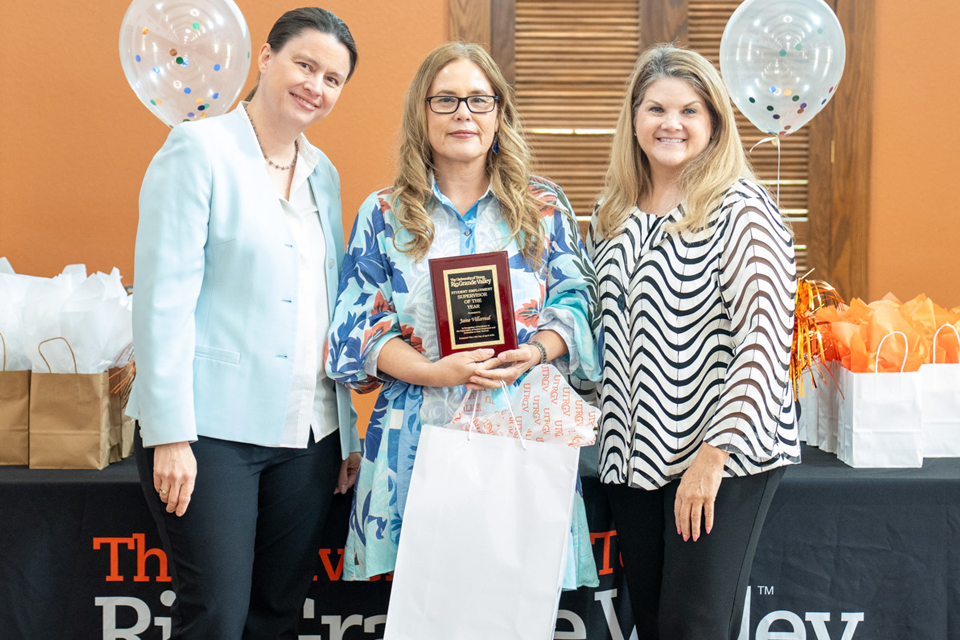 Three persons standing in front of a backdrop that reads UTRGV, one person holding an award