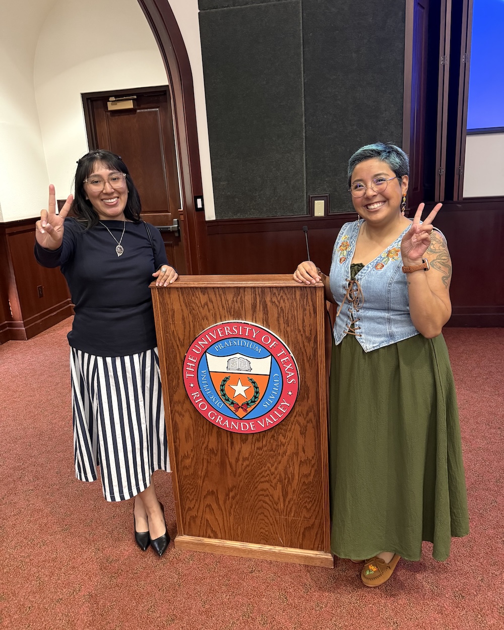 Two people stand indoors beside a wooden podium displaying “The University of Texas Rio Grande Valley” seal.
