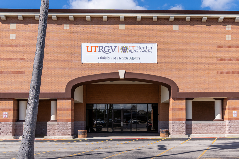 Exterior view of a brick building with a covered entrance and glass doors, featuring a large sign above that reads “UTRGV UT Health Rio Grande Valley Division of Health Affairs.”