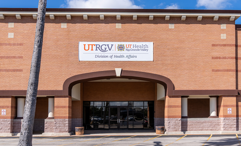 Exterior view of a brick building with a covered entrance and glass doors, featuring a large sign above that reads “UTRGV UT Health Rio Grande Valley Division of Health Affairs.”