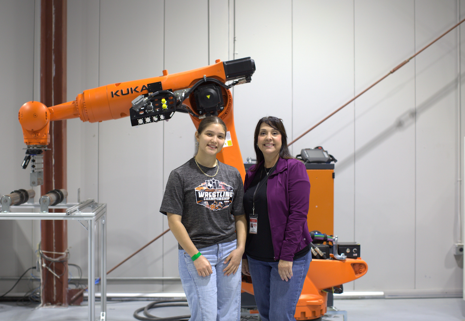 Two people standing next to each other with an orange machine in the background