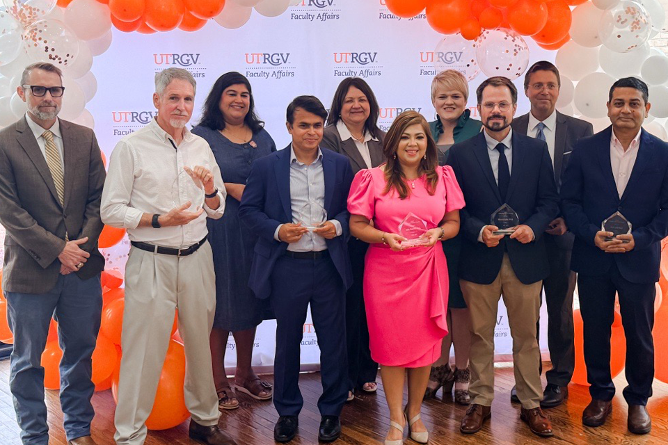 Faculty Impact Award recipients pose for a group photo while holding glass award plaques during a UTRGV Faculty Affairs ceremony. 