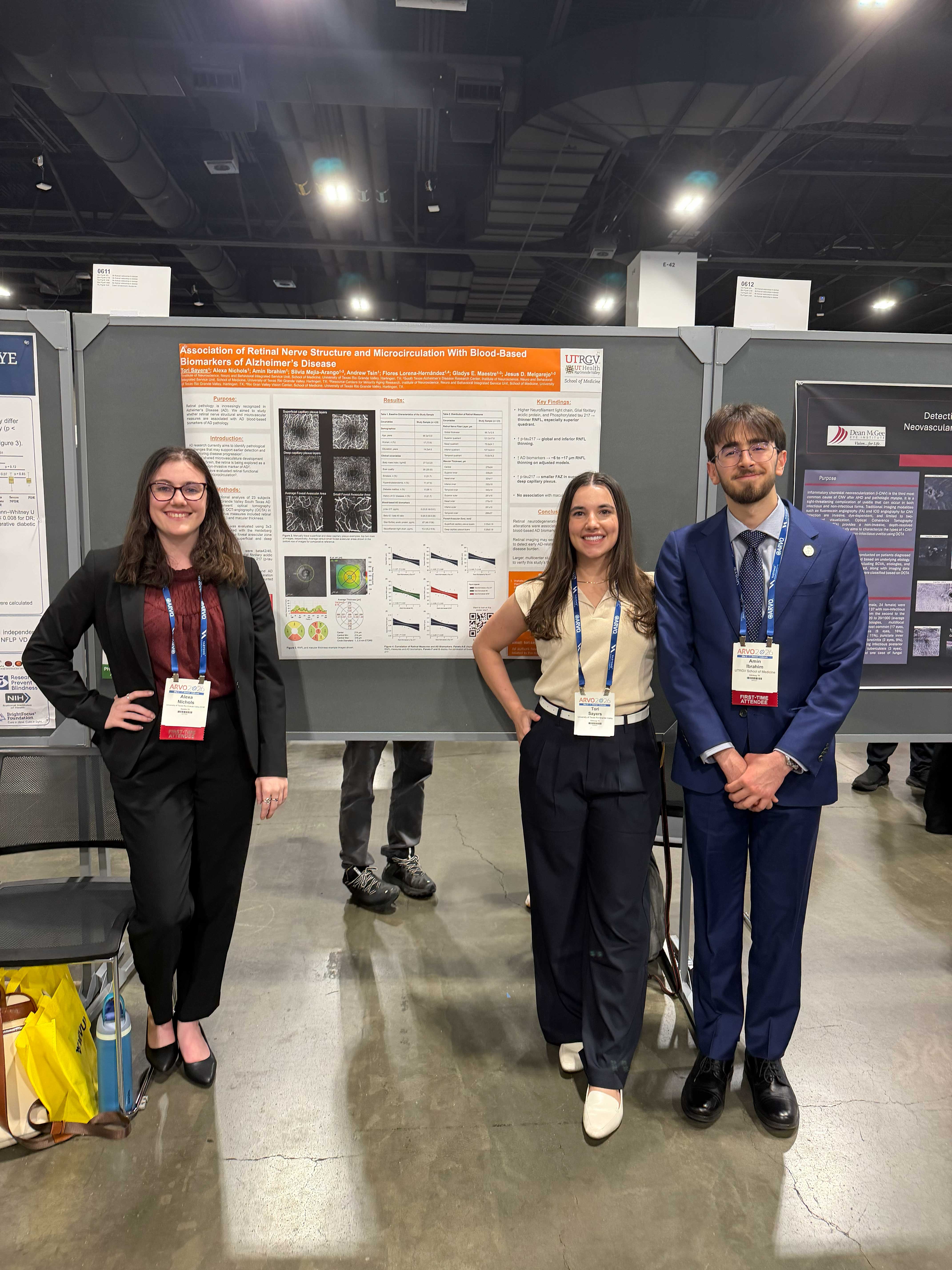 Three people stand in front of a scientific poster at a conference. They appear confident and professional, wearing business attire with badges.