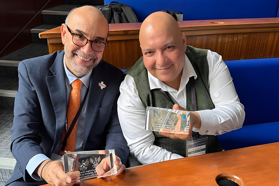 Dr. Javier La Fontaine and Dr. Hooman Mir sit together holding awards received from the Barts and London Surgical Society at the 15th International Surgical Conference in London.