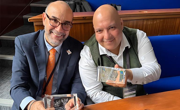 Dr. Javier La Fontaine and Dr. Hooman Mir sit together holding awards received from the Barts and London Surgical Society at the 15th International Surgical Conference in London.
