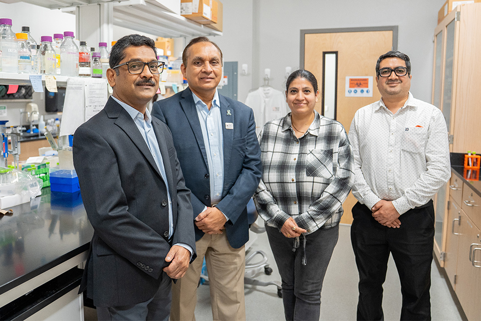 Group of scientists working together in a laboratory, reviewing data and discussing research findings around lab equipment and computer screens. 