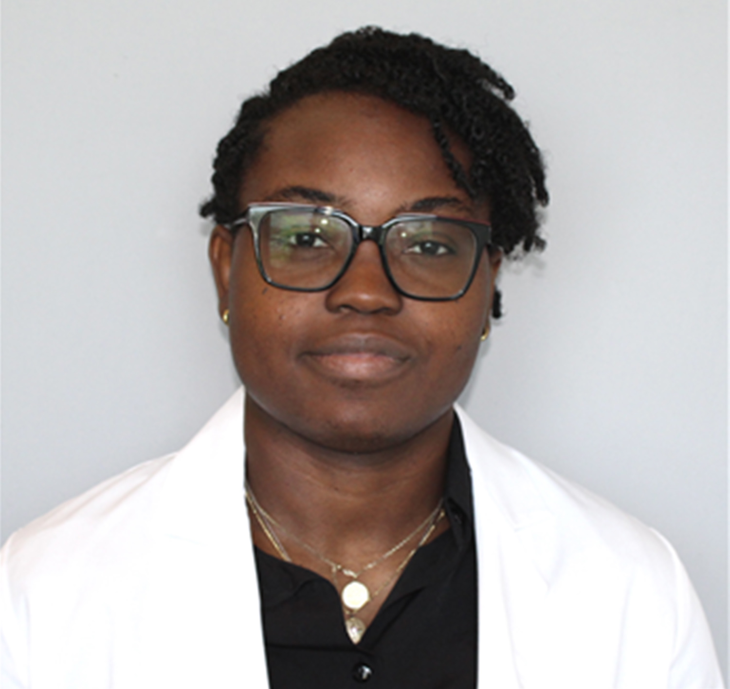 A woman in glasses and a white lab coat, standing confidently in a laboratory setting.