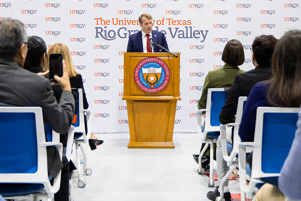 A speaker addresses an audience from a UTRGV podium during a presentation recognizing a $5 million federal grant to support manufacturing in the Rio Grande Valley.