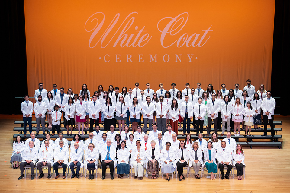 A group of female and male students celebrate the earning of their white coats to become doctors. Faculty and administration join them on stage as well. 