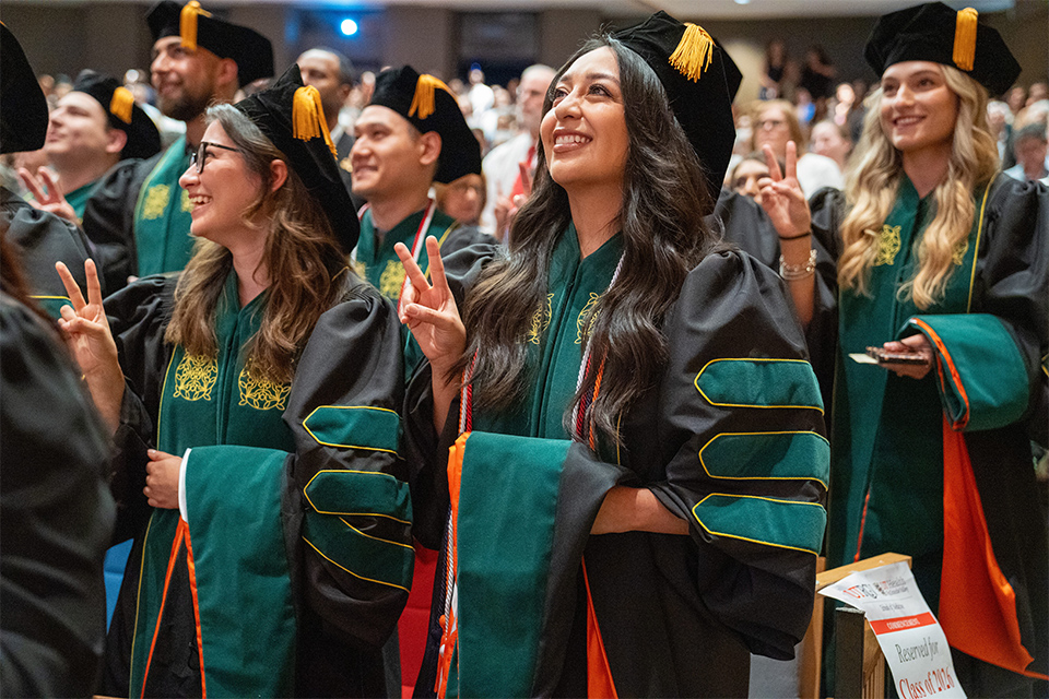 Medical graduates in green-trimmed academic regalia celebrate during a commencement ceremony at the UTRGV Performing Arts Complex.