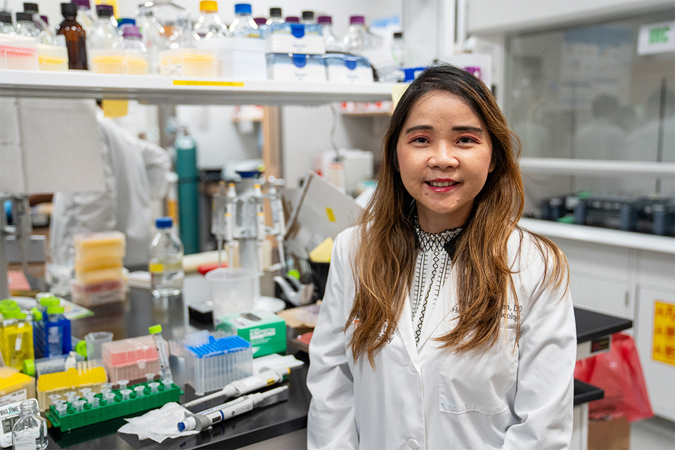 Smiling physician in a lab coat stands in a busy laboratory filled with scientific equipment and colorful reagents, conveying concentration and dedication.