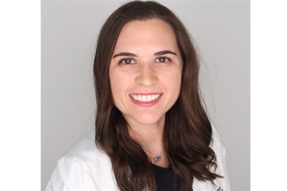 Heather Davis-Lopez smiles for a headshot in a white medical coat against a light gray background.