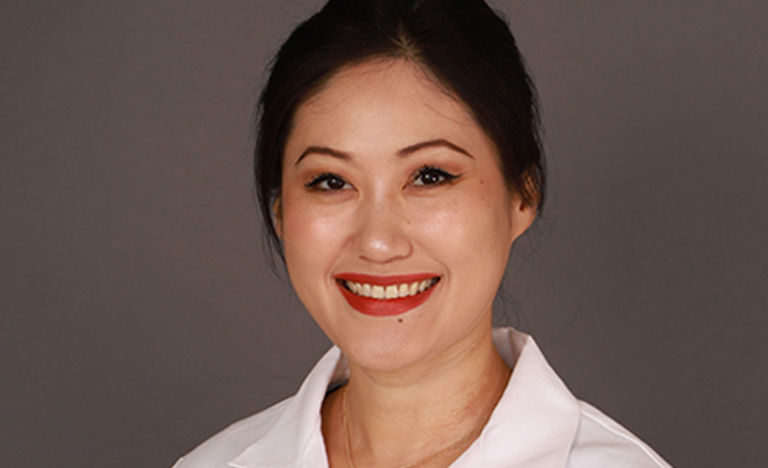 Smiling woman in a white lab coat against a gray ...