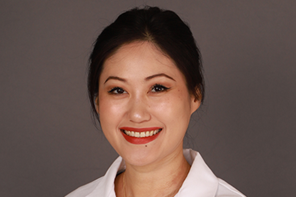 Dr. Juliana Yang, a gastroenterologist, in a white lab coat against a gray background, conveying a professional and friendly tone. The coat has a logo on the left side. and professor of medicine at the UTRGV School of Medicine,