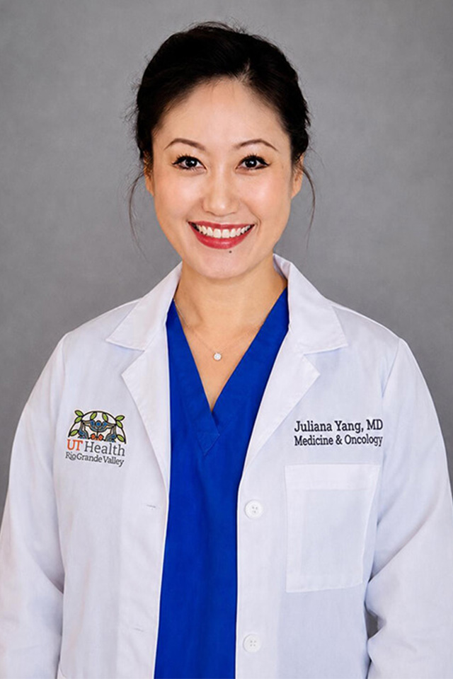 Female wears a white doctors coat as she smiles with a grey background serving as her backdrop.
