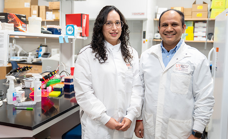 Two lab technicians in white coats stand smiling in a ...