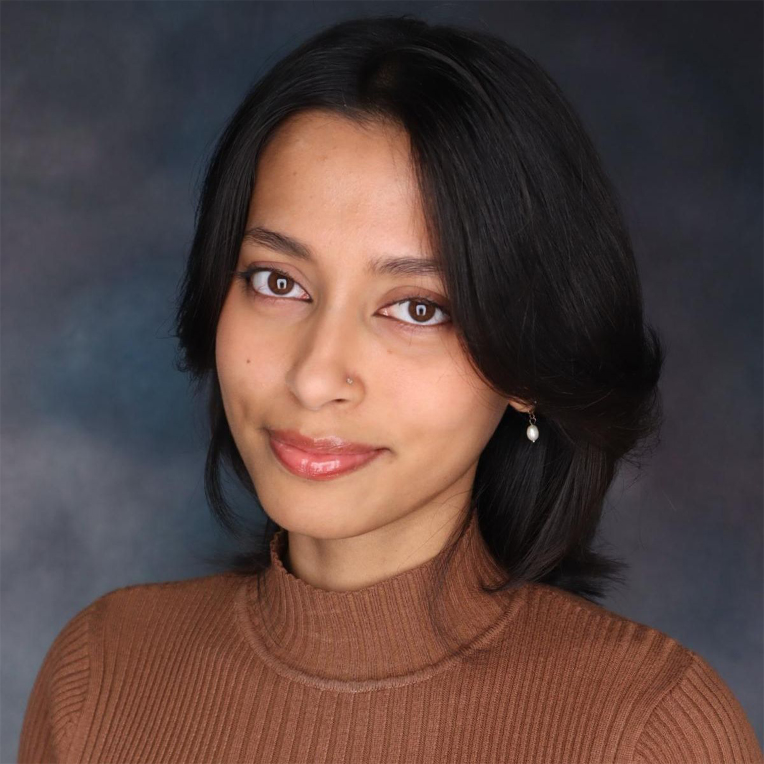 Woman with straight dark hair, brown eyes, wearing a brown turtleneck sweater and a single dangling earring, poses in front of a dark gradient background.