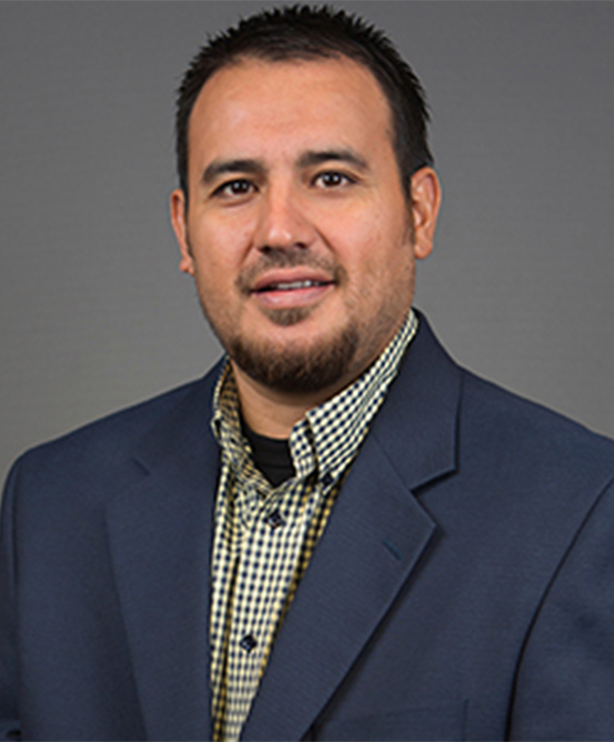 Professional headshot of Dr. Noe Ramos wearing a navy blazer and checkered shirt against a gray background.