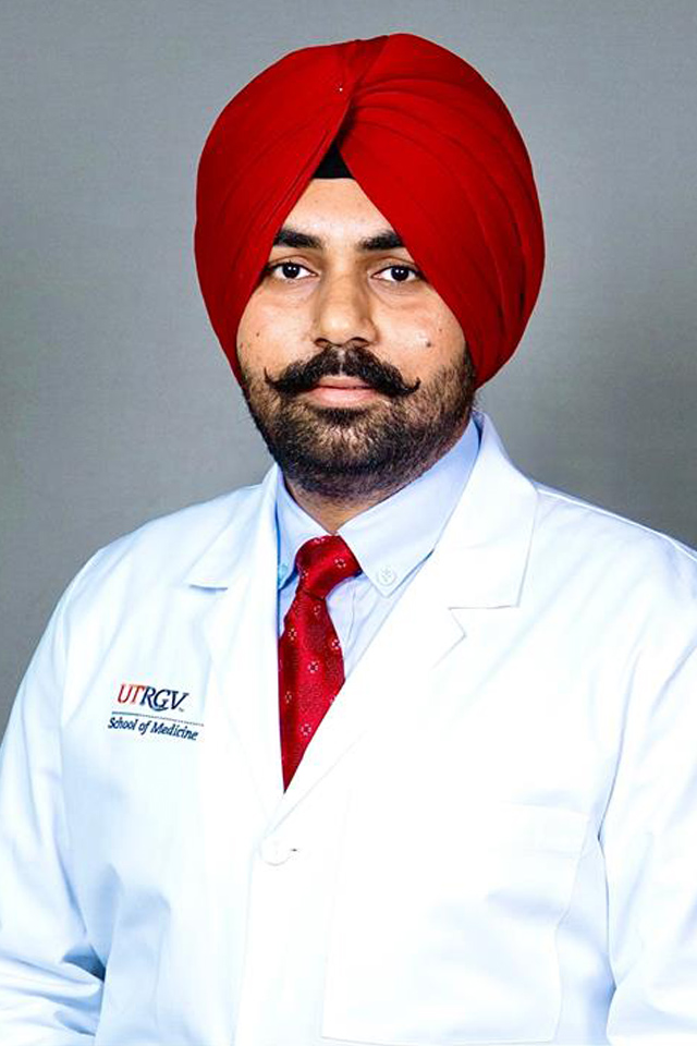 A person wearing a white medical coat embroidered with a UTRGV School of Medicine logo poses against a gray backdrop, dressed with a red tie.