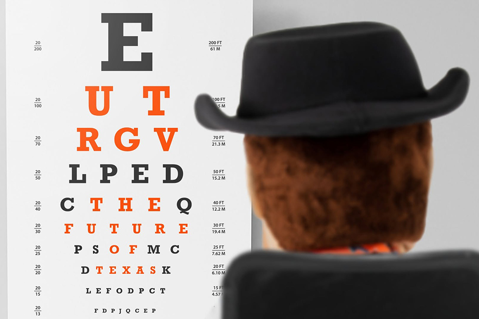 A Snellen eye chart displayed against a light gray background, viewed over the back of a brown plush figure wearing a black cowboy hat. The chart features rows of letters in varying sizes, with key letters highlighted in bold orange that spell out a hidden phrase row-by-row: "UTRGV THE FUTURE OF TEXAS". The remaining letters and measurement ratios appear in standard black text.