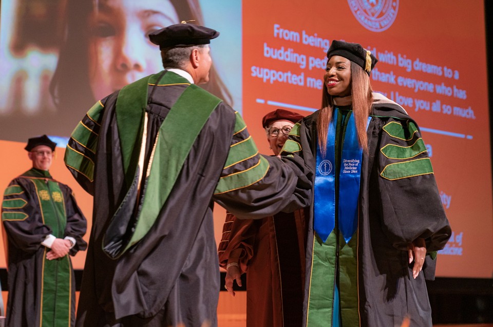 Medical School graduate walks on stage and shakes the hand of professor.