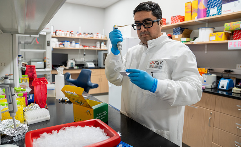 Male in a white lab coat conducts research in lab setting.