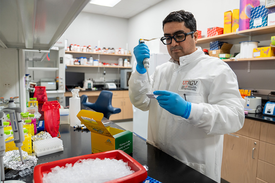 Male in a white lab coat conducts research in lab setting.