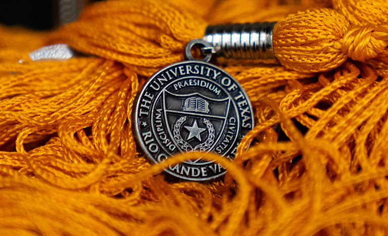 Close-up of orange graduation tassels featuring a silver medallion with The University of Texas Rio Grande Valley seal.