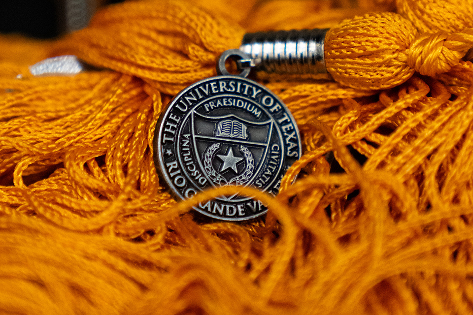 Close-up of orange graduation tassels featuring a silver medallion with The University of Texas Rio Grande Valley seal.