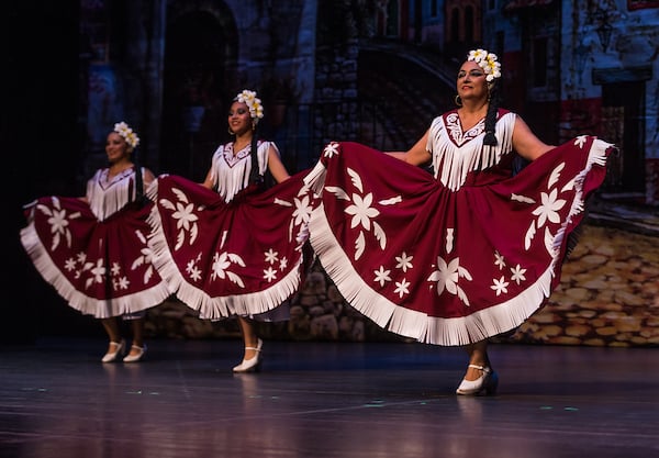 Three folklórico dancers performing on stage.