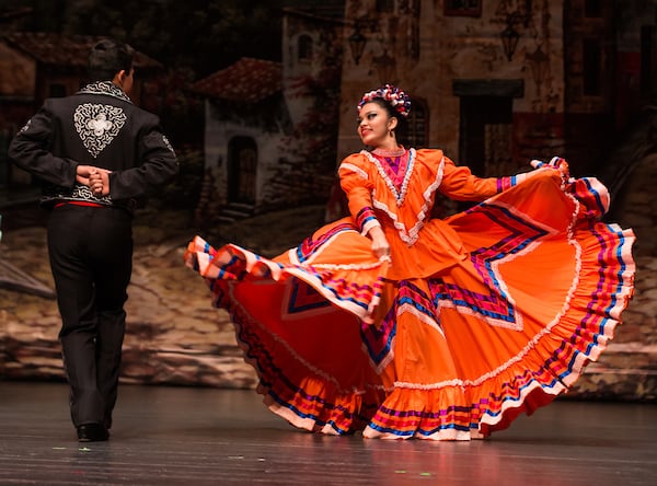 Folklórico dancers take the stage in bright orange colored dresses.