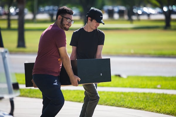 To young men help each other carry a book shelf to the dorm room.