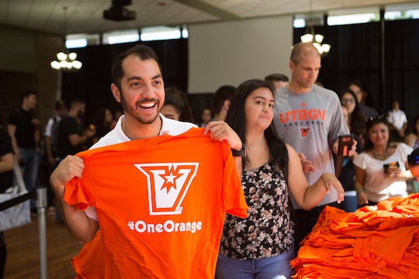 Smiling student holding shirt with Athletic logo and #OneOrange hashtag.