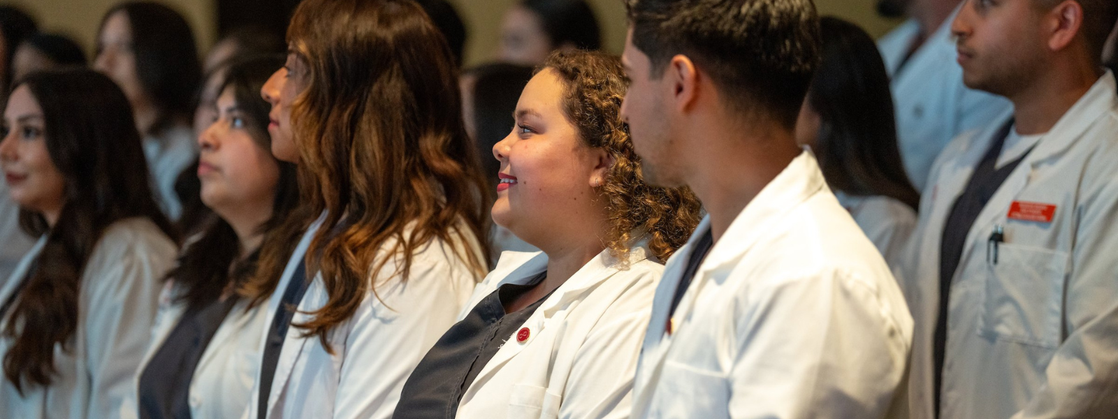 Nursing students in lab coats during pinning event.