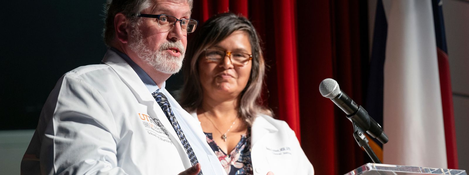Faculty in lab coats standing onstage during ceremony.