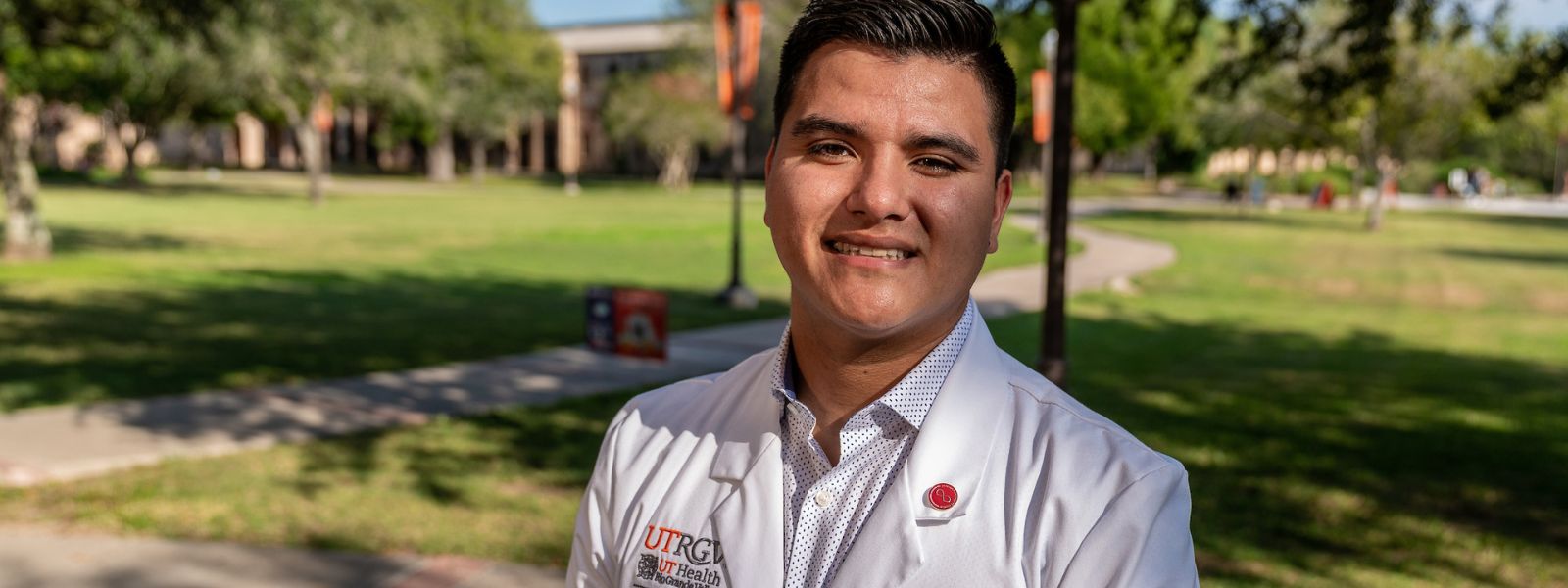Nursing student sitting outdoors while wearing a white coat.