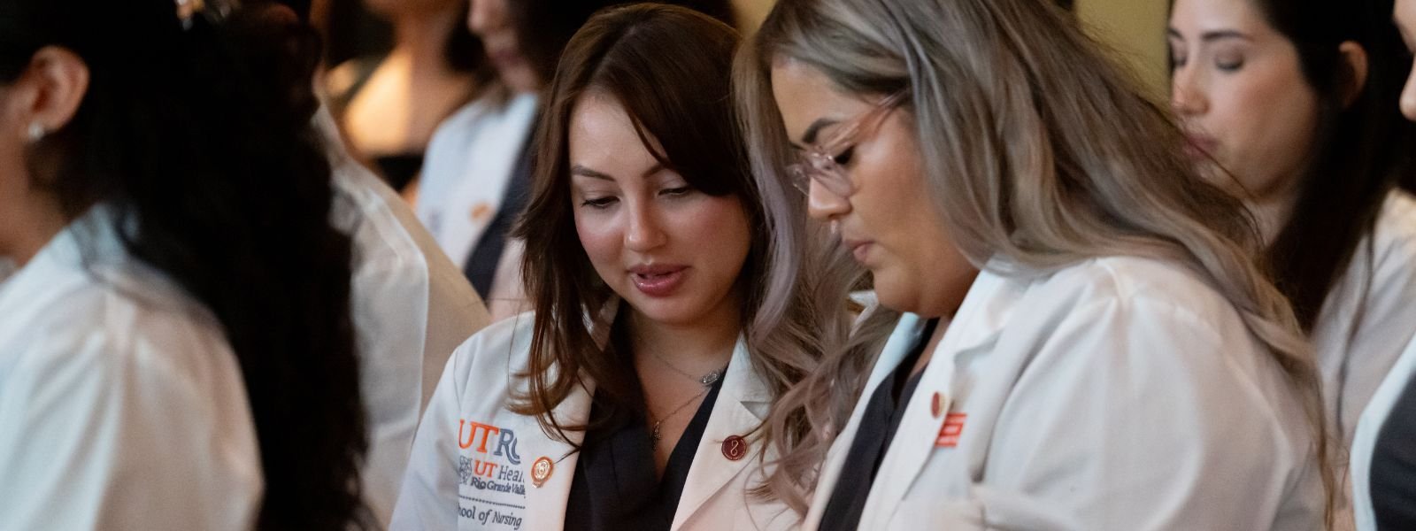 Nursing students during ceremony wearing white coats..