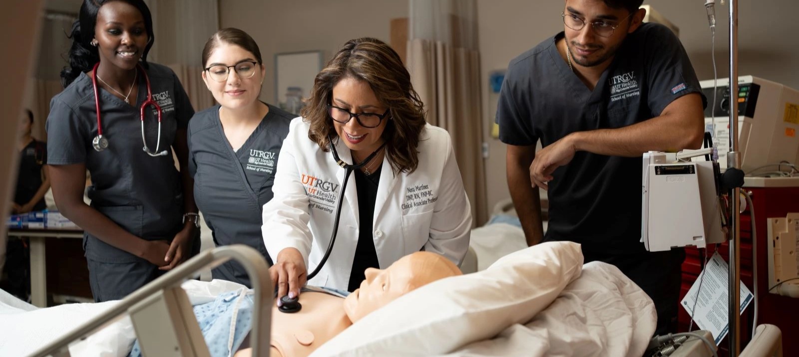 Faculty demonstrating how to use a stethoscope to check a manikin’s heartbeat.