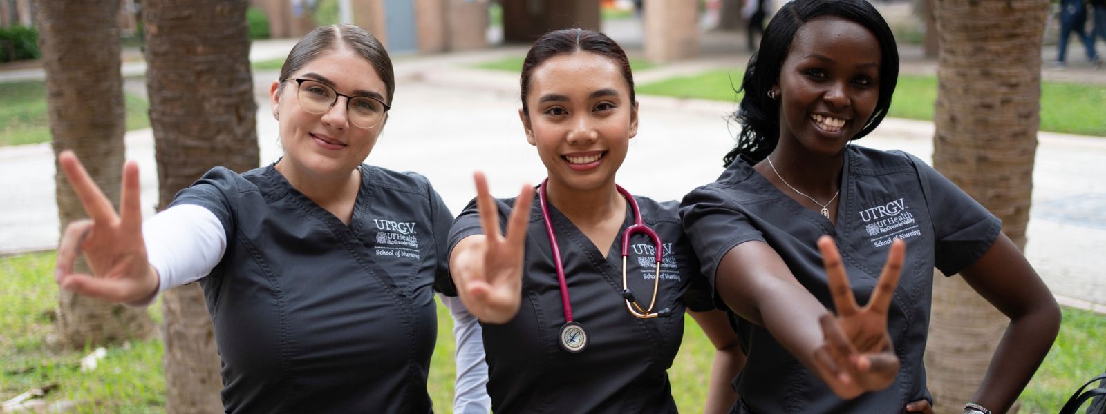 Nursing students in gray scrubs signaling v's up.