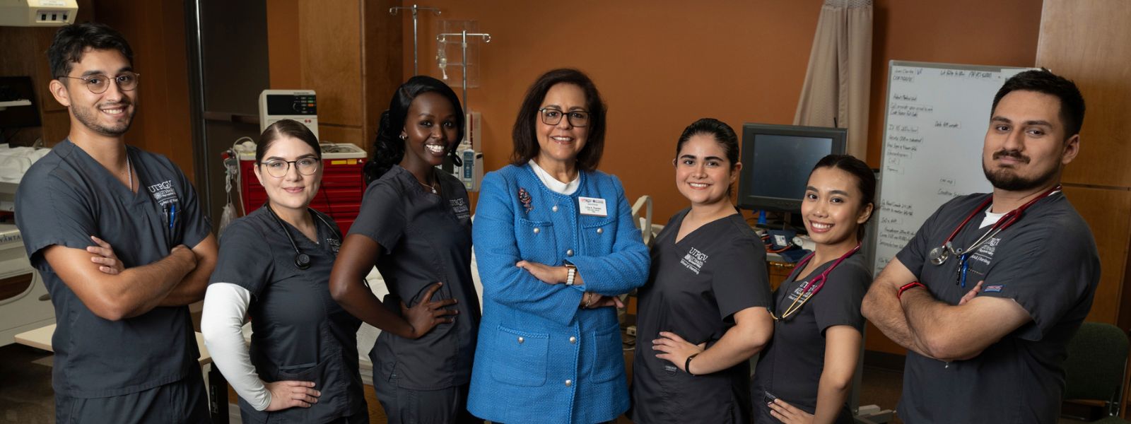 Nursing students in gray scrubs posing for photo with Nursing dean in the center.