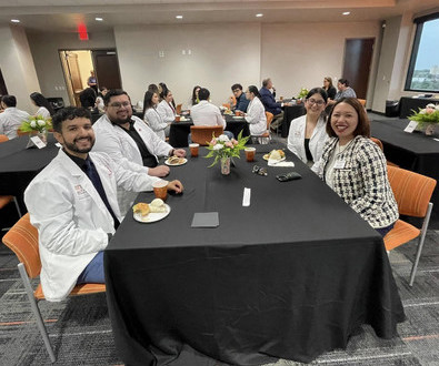 Group of students in white coats during ceremony sitting at a table.