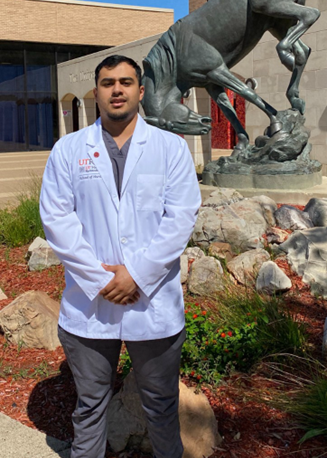Student in white coat posing for photo while standing next to university's horse.