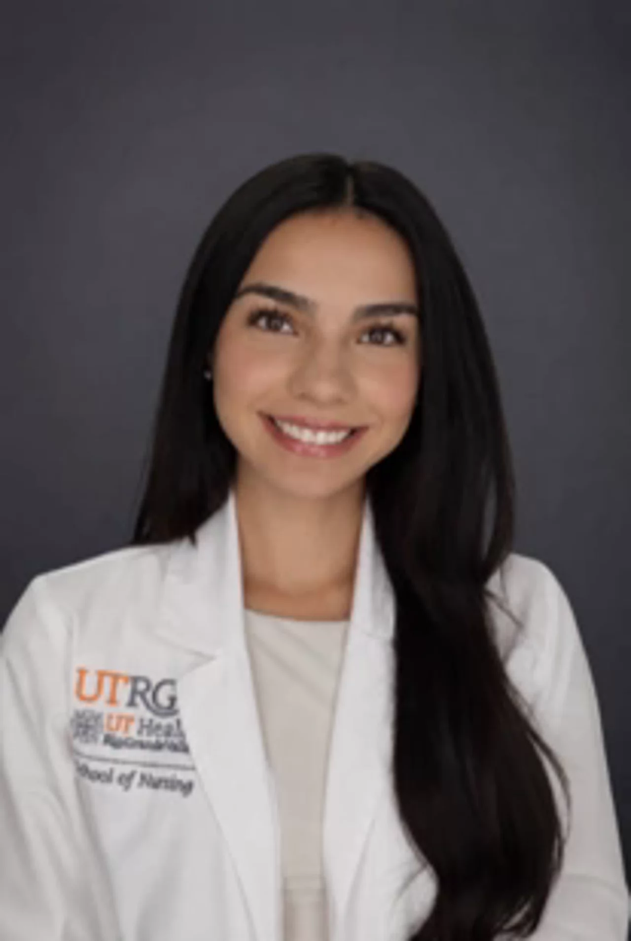 Portrait of Alexandra Diaz wearing a white UTRGV School of Nursing lab coat, smiling at the camera against a plain background.