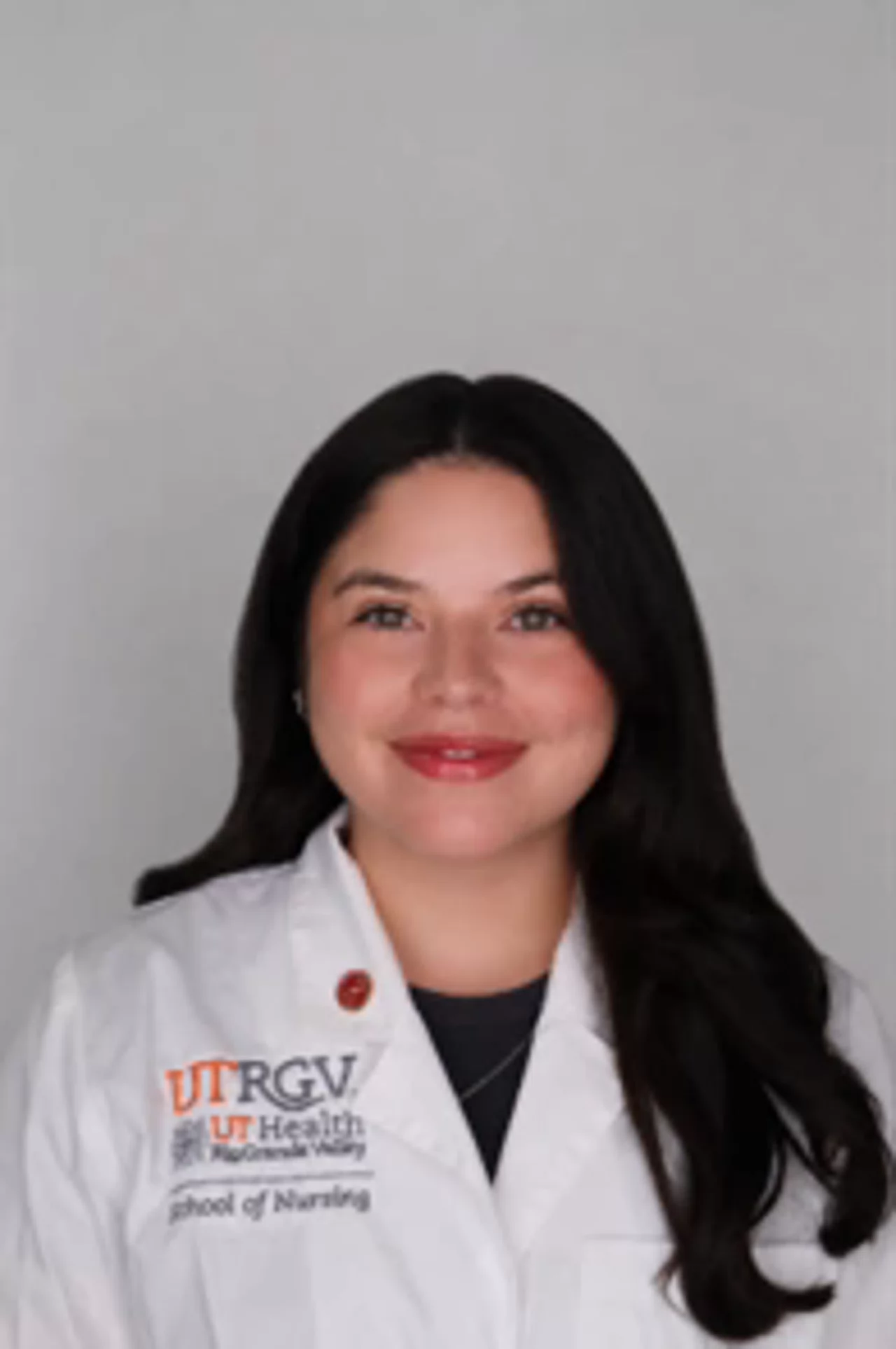 Portrait of Amanda Contreras wearing a white UTRGV School of Nursing lab coat, smiling at the camera against a light background.