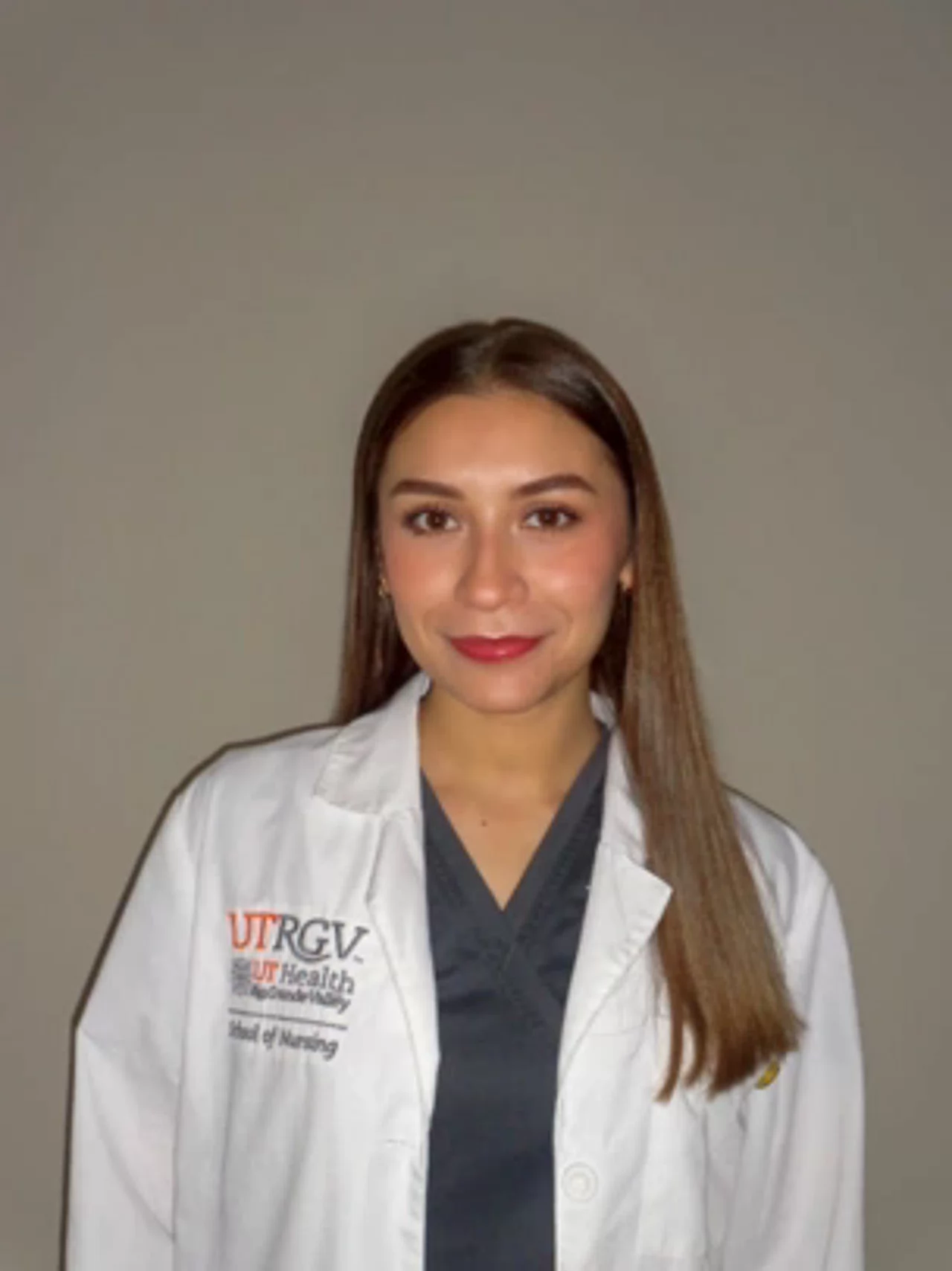Portrait of Camila Hinojosa wearing a white UTRGV School of Nursing lab coat, smiling at the camera against a neutral background.