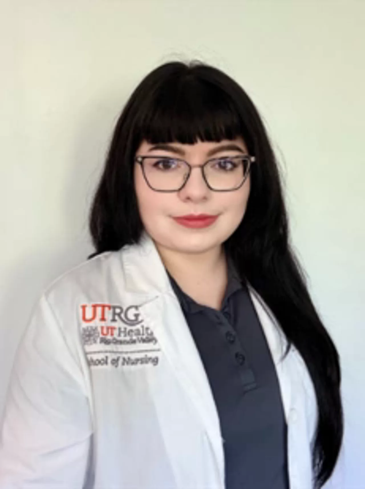 Portrait of Catherine Clark wearing a white UTRGV School of Nursing lab coat, facing the camera against a light background.