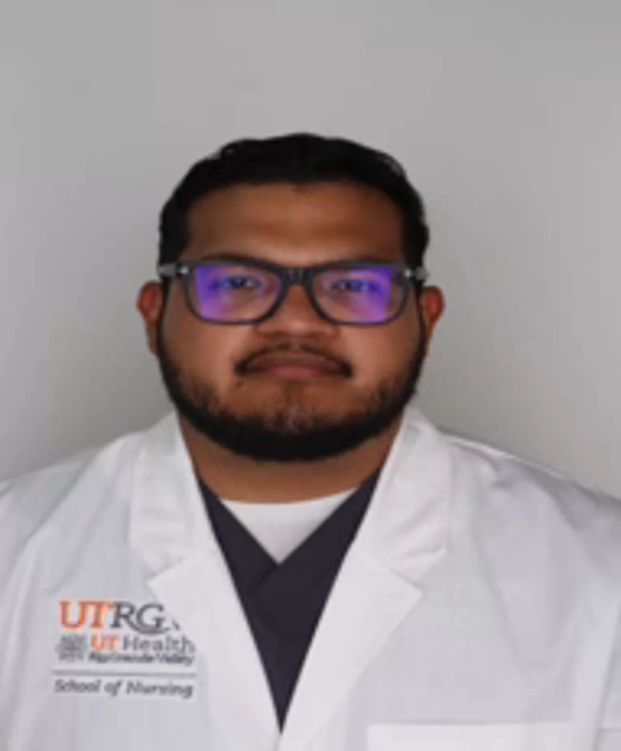 Portrait of Eduardo Ramirez wearing a white UTRGV School of Nursing lab coat, facing the camera against a light background.