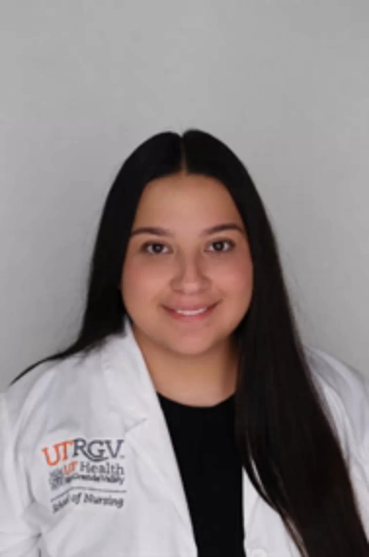 Portrait of Evelyn Trigo wearing a white UTRGV School of Nursing lab coat, smiling at the camera against a neutral background.
